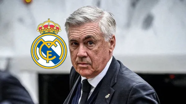 Carlo Ancelotti looks at the camera while wearing a suit and the Real Madrid logo is next to him.