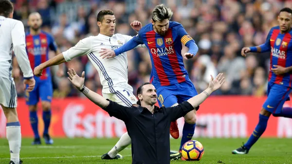 Cristiano Ronaldo and Lionel Messi contest for the ball at the same time and Zlatan Ibrahimovic extends his arms out with a smile.
