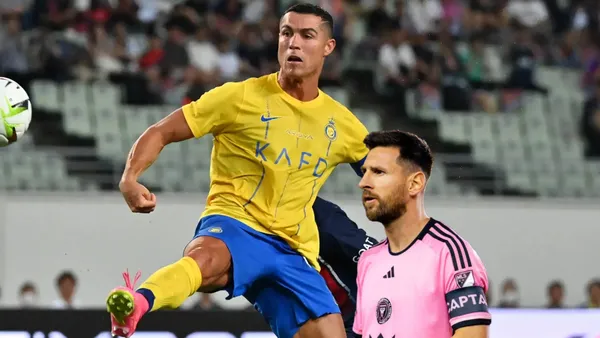 Cristiano Ronaldo looks at the ball while wearing the Al Nassr jersey and Lionel Messi stares while wearing the Inter Miami jersey.