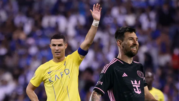Cristiano Ronaldo raises his hand while Lionel Messi smiles wearing an Inter Miami shirt.