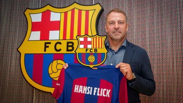 Hansi Flick holds the FC Barcelona jersey with his name on it and the FC Barcelona badge is in the middle.