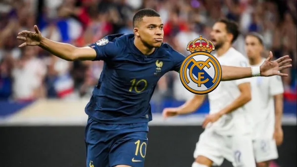 Kylian Mbappé celebrates a France goal with his arms out while wearing the blue France national team jersey; the Real Madrid badge is next to him.