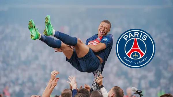 Kylian Mbappé smiles in the air as he is thrown by his PSG teammates; the PSG badge is next to him.