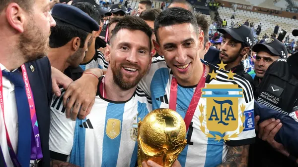 Lionel Messi and Angel Di Maria pose for a picture together with the World Cup trophy and the Argentina national team badge is next to them.