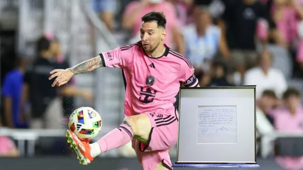 Lionel Messi touches the ball with his foot wearing an Inter Miami kit while his napkin contract is next to him.