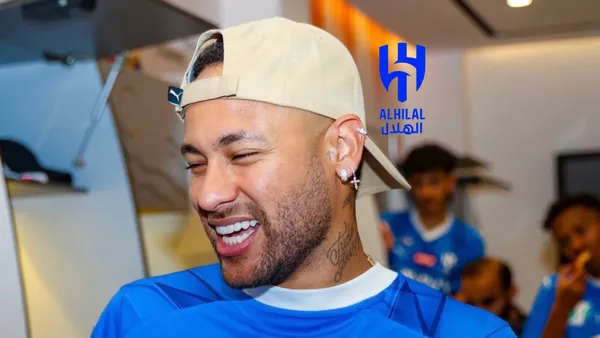 Neymar smiles while wearing a hat and the Al Hilal jersey. The Al Hilal badge is next to him.