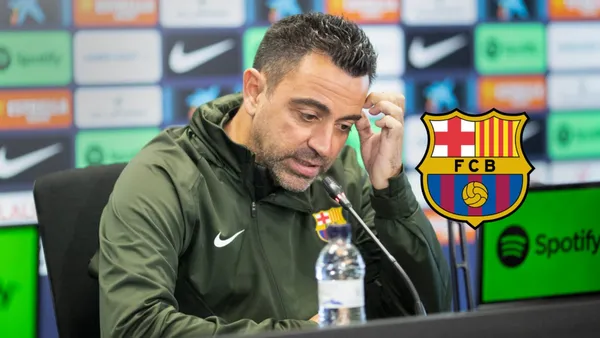 Xavi Hernandez scratches his head during a press conference while the FC Barcelona badge is next to him.